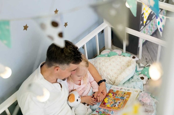 Young father dad in bed with 3-year-old daughter reading a book at bedtime. View from above. Focus on hands