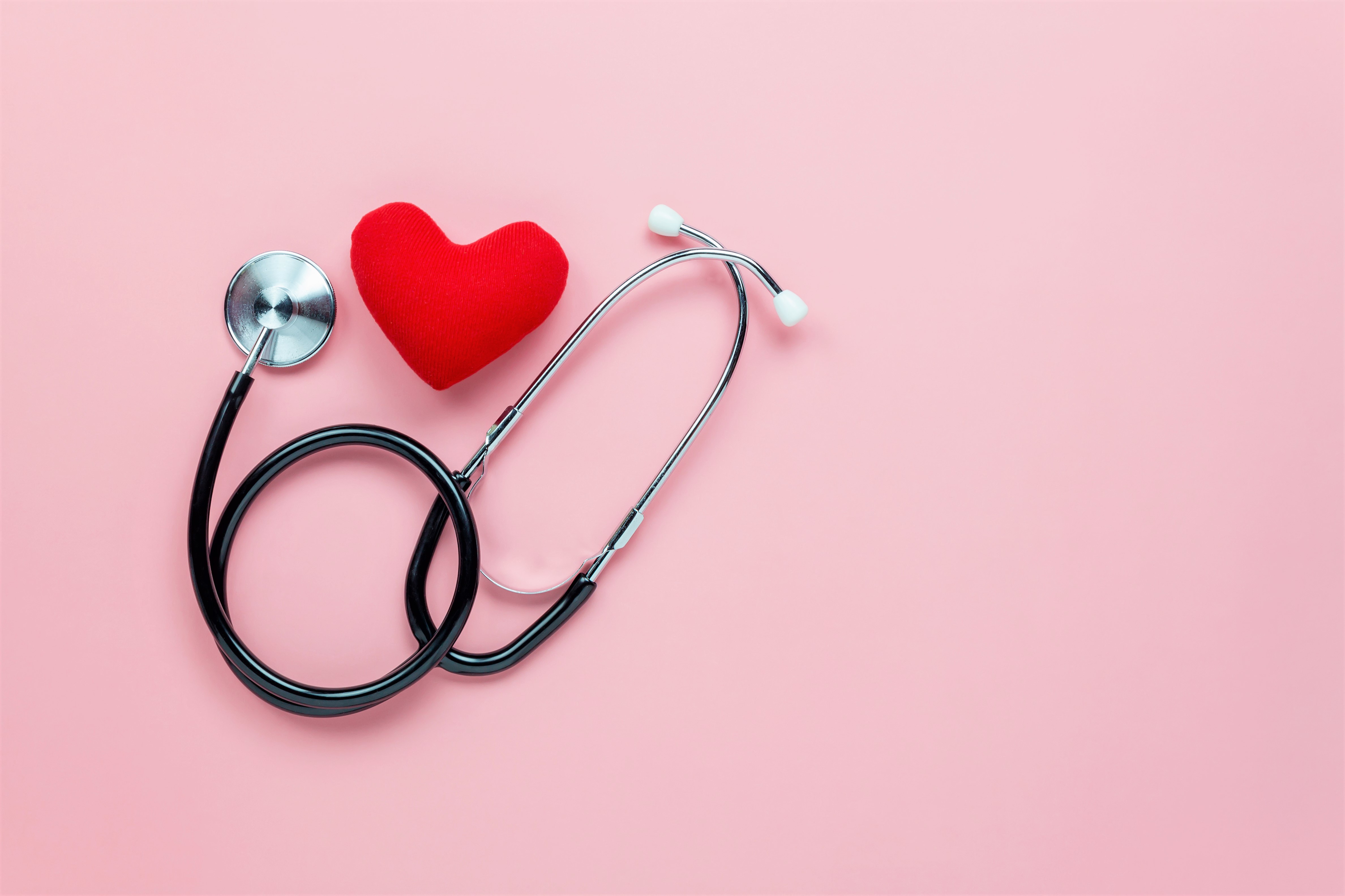 Black Stethoscope Wrapped Around Red Heart Over Pink Background