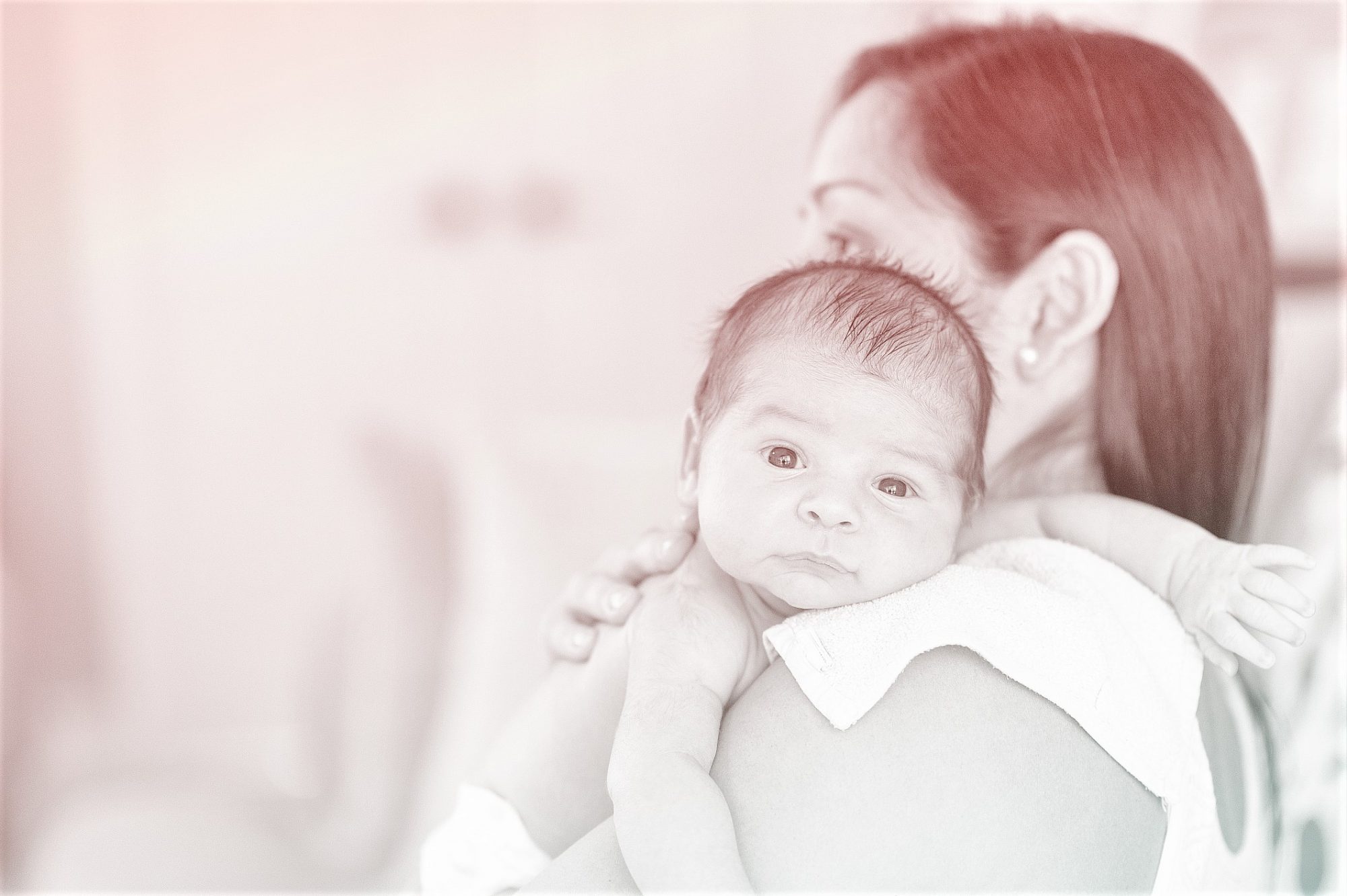 mother holds newborn baby over her shoulder at home