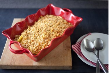 Squash casserole in a red fluted baking dish, displayed on a wooden cutting board alongside white side plates and spoons