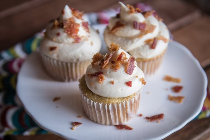 Cupcakes on a white plate, mounded with off-white frosting and sprinkled with crumbled bacon bits