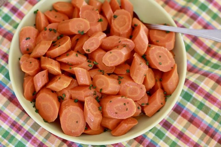 Overhead shot of maple-glazed carrots in a pale green bowl, on a colorful patterned tablecloth