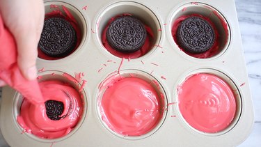 Piping melted red chocolate on top of Oreos