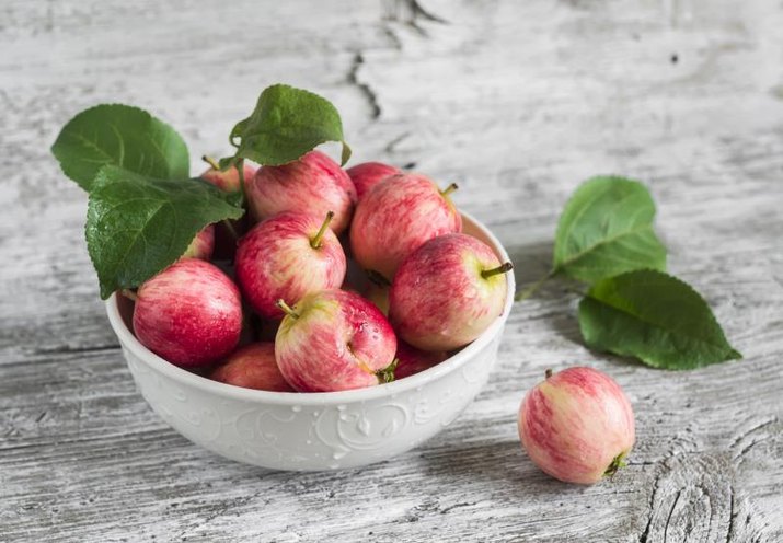 fresh red apples in a white bowl on a light wooden surface