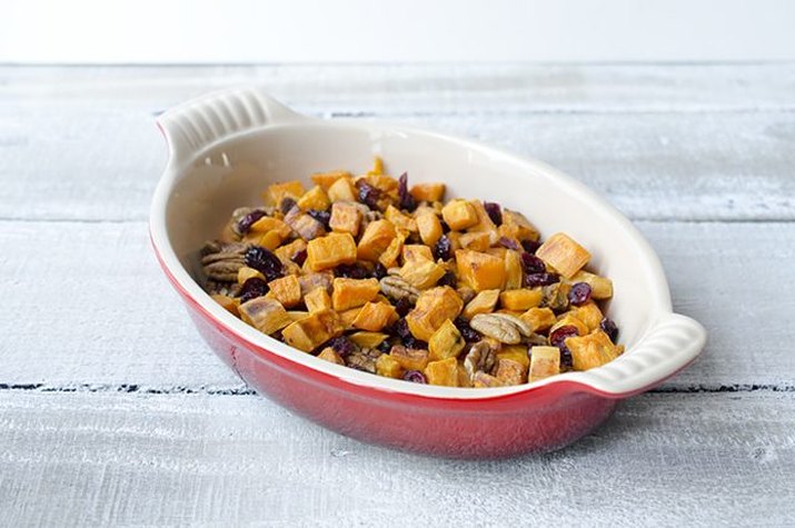 A dish filled with roasted sweet potatoes, cranberries and pecans.