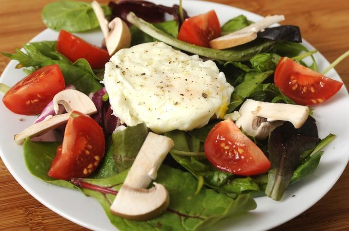 A seasoned poached egg served on top of a bed of salad.