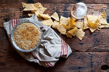 A freshly baked dish of jalapeno popper beer cheese dip beside tortilla chips and a beer.