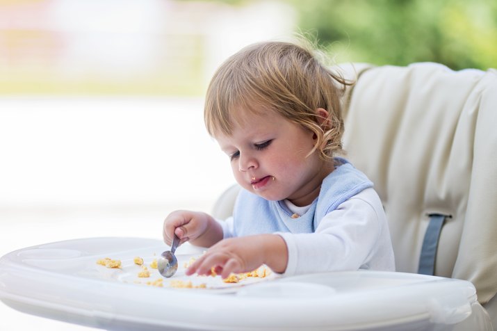 Cute baby eating breakfast in high chair.