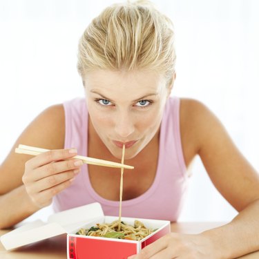 woman eating noodles from a take-out box with chopsticks